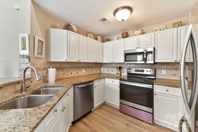 kitchen with stainless steel appliances, light stone countertops, sink, and white cabinets