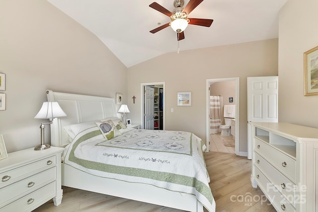 bedroom with ceiling fan, a walk in closet, ensuite bathroom, light hardwood / wood-style floors, and vaulted ceiling