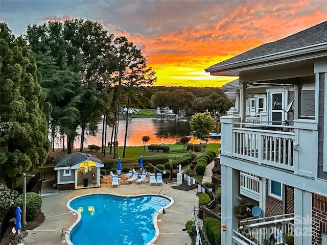 pool at dusk with a water view, a patio, and an outbuilding