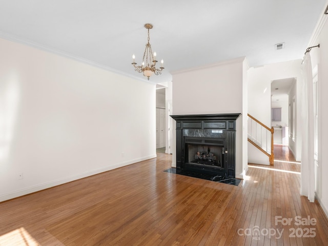 unfurnished living room with hardwood / wood-style floors, crown molding, a fireplace, and a notable chandelier