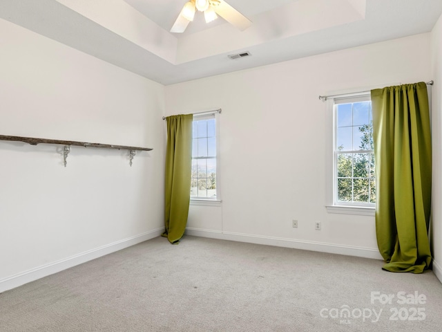 empty room featuring a raised ceiling, light colored carpet, and ceiling fan