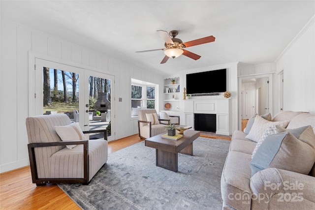 living room with crown molding, built in shelves, wood-type flooring, and ceiling fan