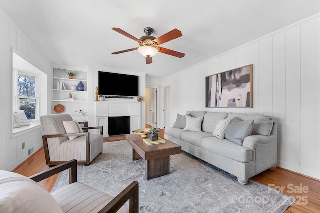 living room featuring crown molding, wood-type flooring, built in features, and ceiling fan