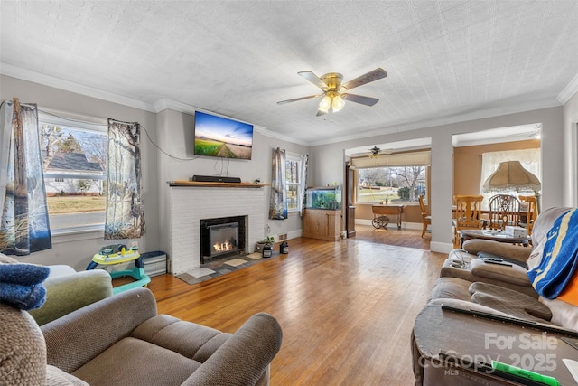 living area featuring ornamental molding, a fireplace, wood finished floors, and baseboards