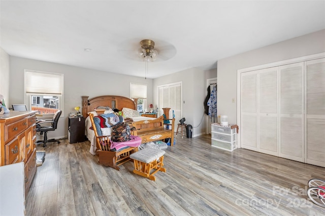 bedroom with light wood finished floors, two closets, a ceiling fan, and baseboards