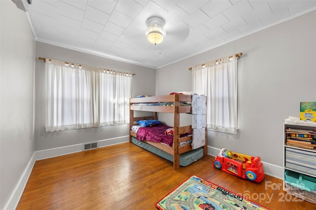 bedroom featuring ornamental molding, wood finished floors, visible vents, and baseboards