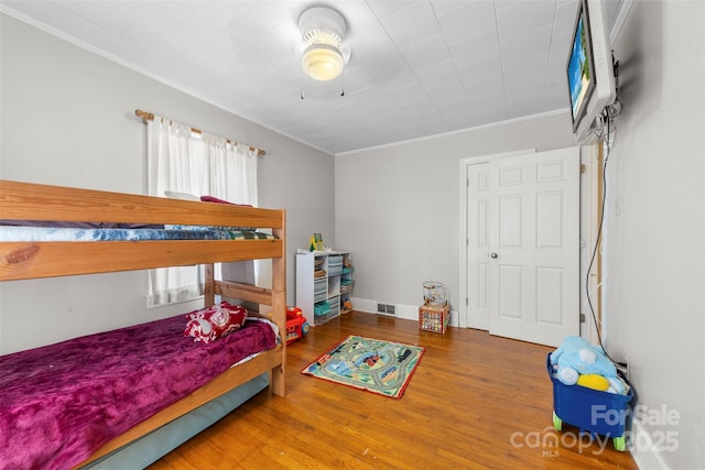 bedroom with baseboards, crown molding, visible vents, and wood finished floors