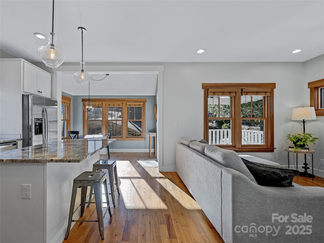 kitchen with stainless steel refrigerator with ice dispenser, pendant lighting, white cabinets, a kitchen bar, and dark stone countertops