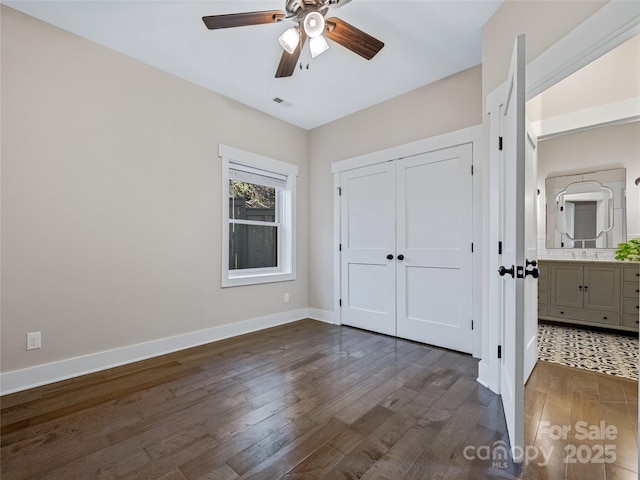 unfurnished bedroom featuring dark wood-type flooring, ensuite bathroom, a closet, and ceiling fan