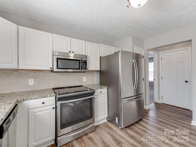 kitchen featuring backsplash, stainless steel appliances, light stone counters, light hardwood / wood-style floors, and white cabinets