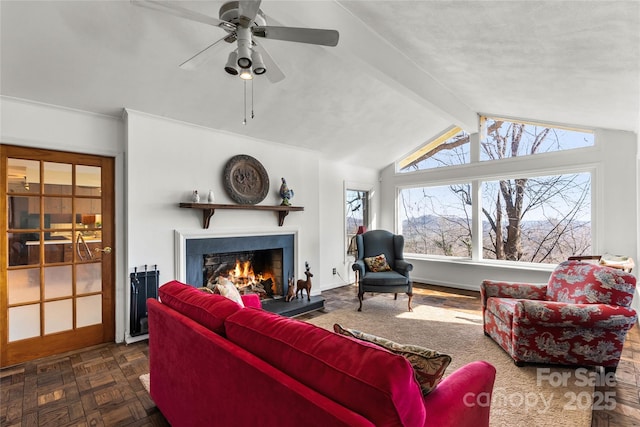 living area with lofted ceiling with beams, a lit fireplace, baseboards, and a ceiling fan