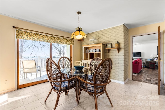 dining room with light tile patterned floors, brick wall, ornamental molding, and baseboards