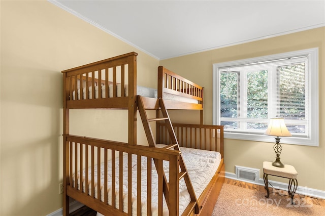 bedroom with baseboards, visible vents, wood finished floors, and ornamental molding