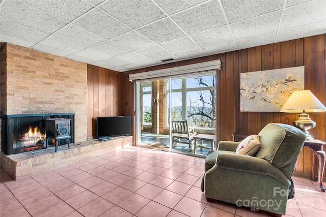 unfurnished living room featuring tile patterned flooring, a brick fireplace, visible vents, and wood walls