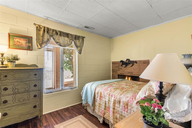 bedroom featuring dark wood-type flooring, a brick fireplace, visible vents, and concrete block wall