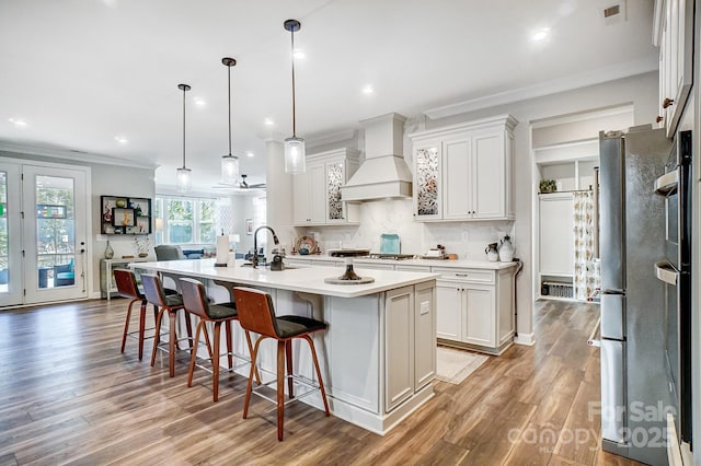 kitchen with white cabinetry, hanging light fixtures, a center island with sink, and premium range hood