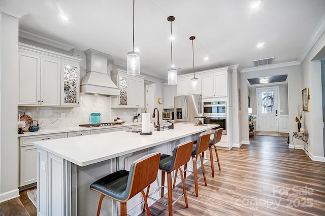 kitchen with tasteful backsplash, visible vents, custom range hood, stainless steel appliances, and a sink