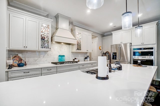 kitchen featuring custom exhaust hood, stainless steel appliances, hanging light fixtures, light countertops, and decorative backsplash