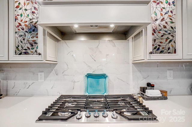 kitchen with decorative backsplash, custom exhaust hood, stainless steel gas stovetop, and light countertops