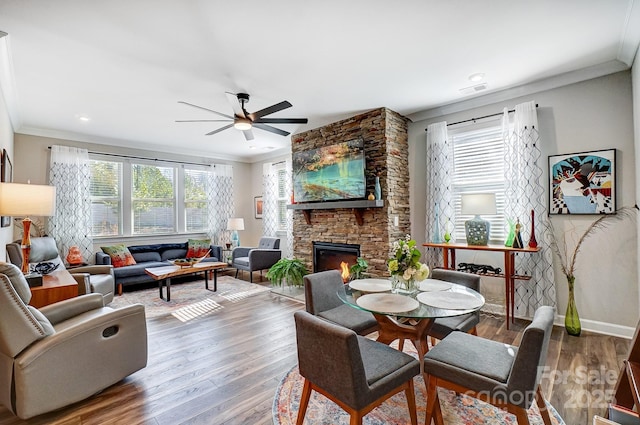 living area featuring a stone fireplace, wood finished floors, a ceiling fan, and ornamental molding