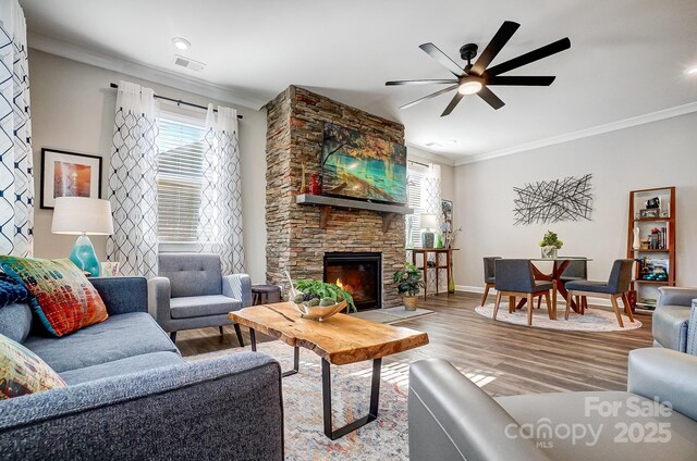 living room featuring a stone fireplace, crown molding, wood finished floors, and visible vents