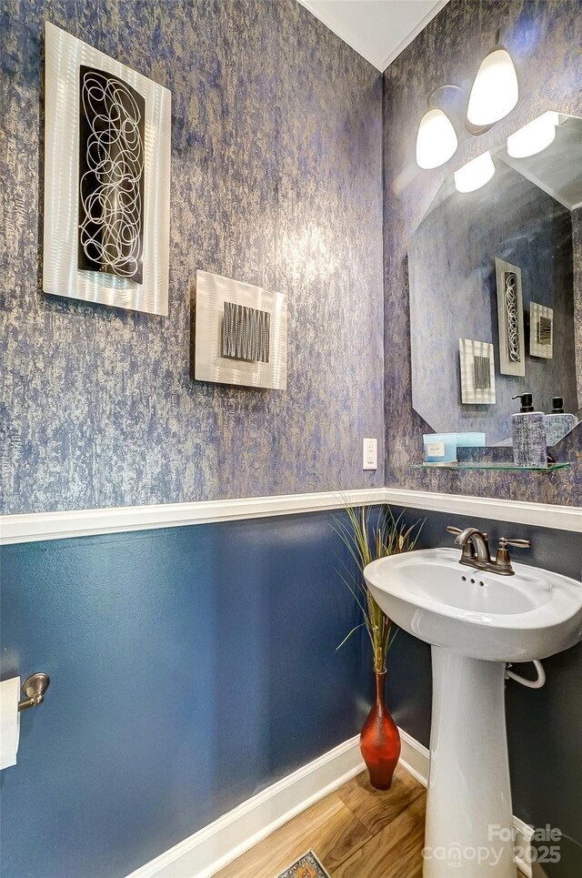 bathroom featuring wallpapered walls, wood finished floors, baseboards, and a sink