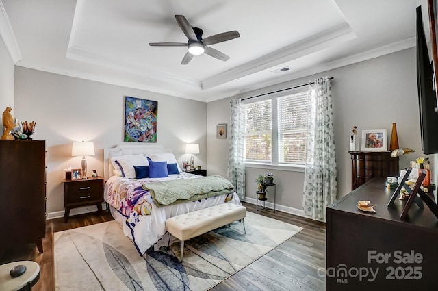 bedroom with visible vents, a ceiling fan, a tray ceiling, wood finished floors, and baseboards