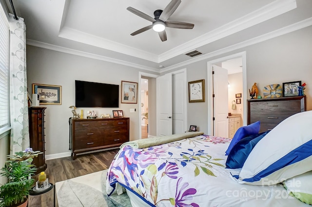 bedroom with visible vents, ensuite bathroom, a tray ceiling, and wood finished floors