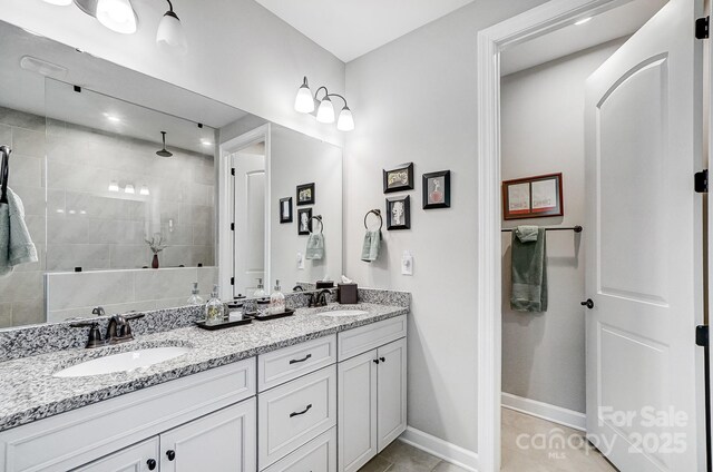 full bath with double vanity, baseboards, a tile shower, and a sink