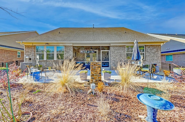 back of property featuring fence, brick siding, roof with shingles, and a patio area