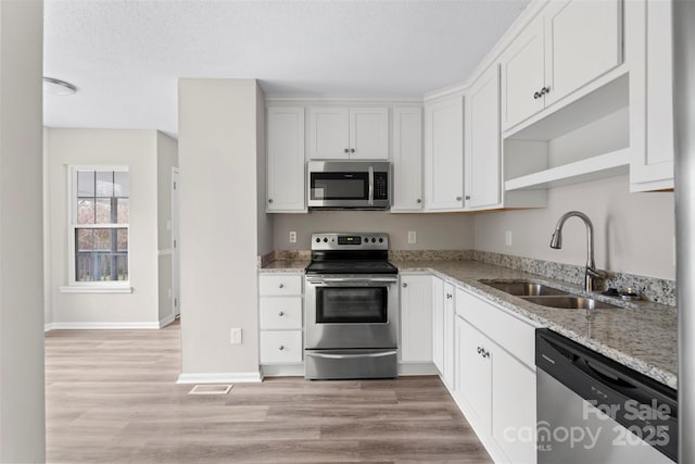 kitchen with appliances with stainless steel finishes, sink, white cabinets, light wood-type flooring, and light stone countertops