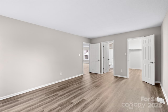 unfurnished bedroom with a walk in closet, ensuite bath, light wood-type flooring, and a closet