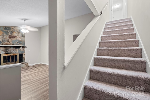 stairway featuring hardwood / wood-style flooring, a textured ceiling, and a stone fireplace