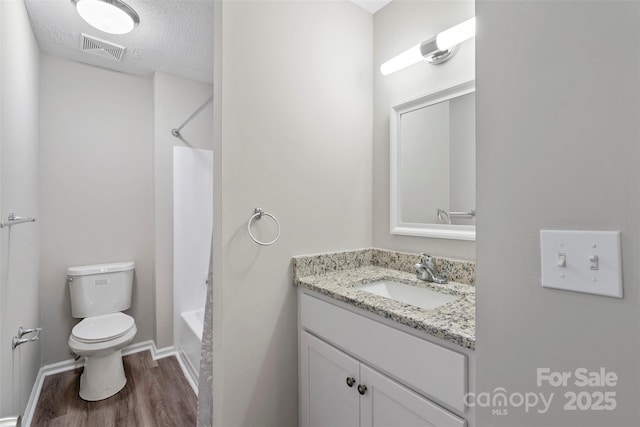 full bathroom featuring hardwood / wood-style floors, toilet, a textured ceiling, vanity, and washtub / shower combination