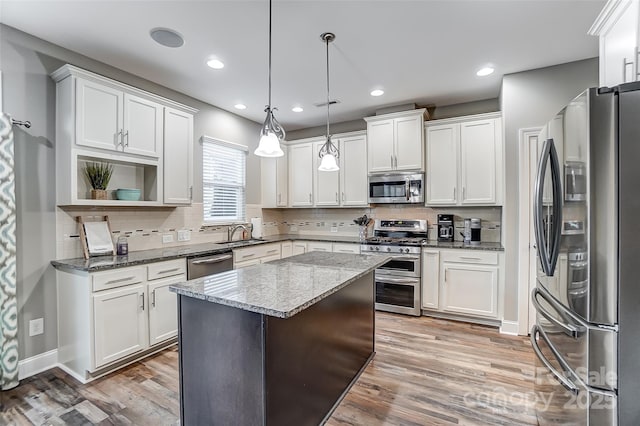 kitchen with appliances with stainless steel finishes, pendant lighting, sink, dark stone countertops, and white cabinets