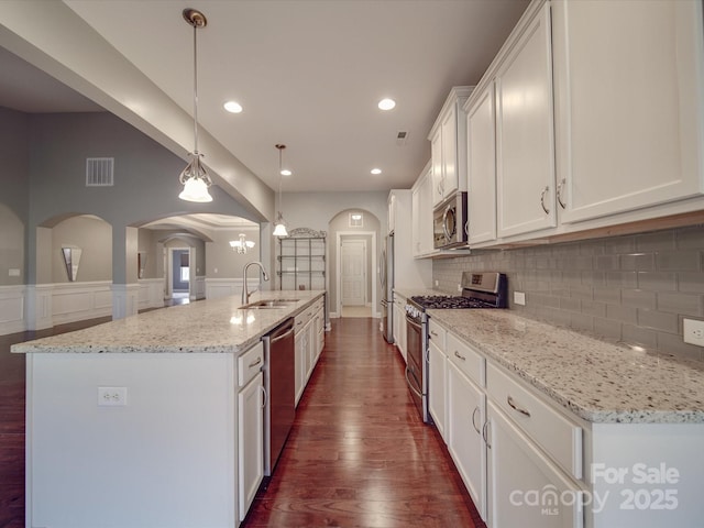 kitchen with sink, hanging light fixtures, appliances with stainless steel finishes, an island with sink, and white cabinets