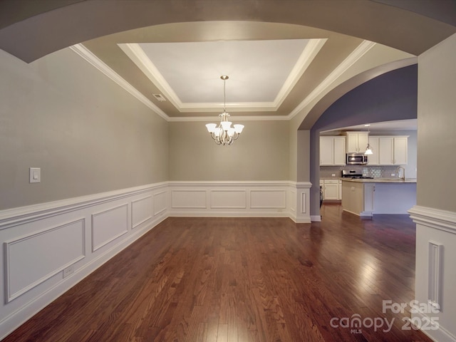 unfurnished dining area featuring sink, a chandelier, dark hardwood / wood-style flooring, ornamental molding, and a tray ceiling