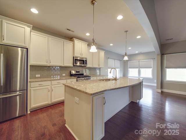 kitchen with pendant lighting, sink, stainless steel appliances, an island with sink, and white cabinets