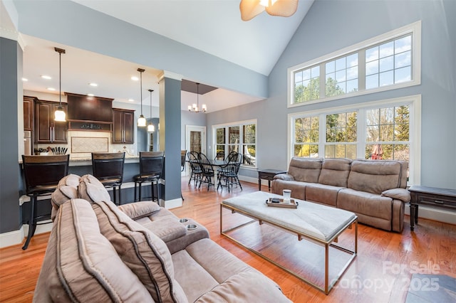 living room featuring ceiling fan with notable chandelier, light hardwood / wood-style flooring, and high vaulted ceiling