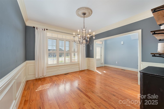 unfurnished dining area with a notable chandelier, crown molding, and light hardwood / wood-style floors