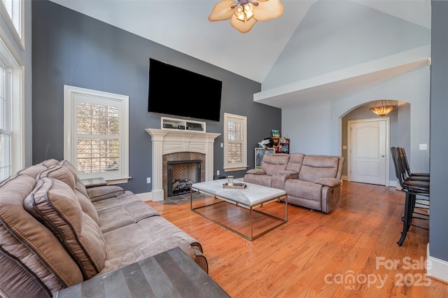 living room with ceiling fan, a fireplace, high vaulted ceiling, and light wood-type flooring