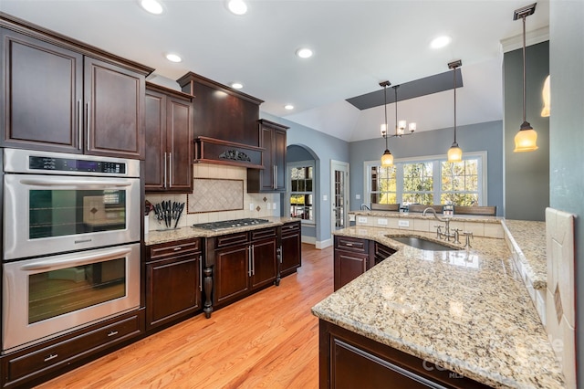 kitchen with decorative light fixtures, sink, light stone counters, dark brown cabinetry, and stainless steel appliances