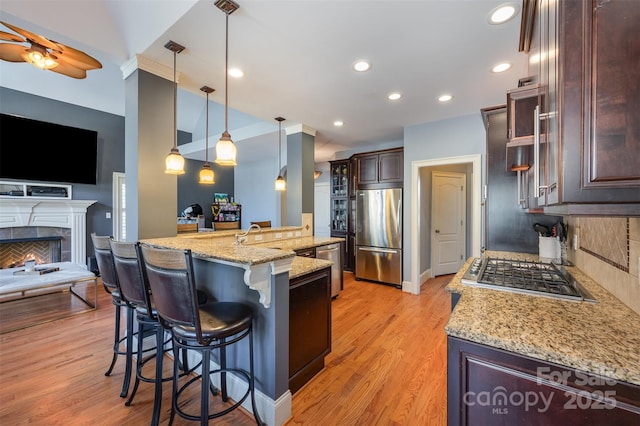 kitchen with appliances with stainless steel finishes, decorative light fixtures, a kitchen breakfast bar, a kitchen island with sink, and light hardwood / wood-style flooring