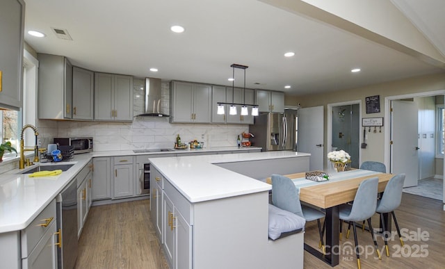 kitchen featuring sink, appliances with stainless steel finishes, a kitchen island, pendant lighting, and wall chimney range hood