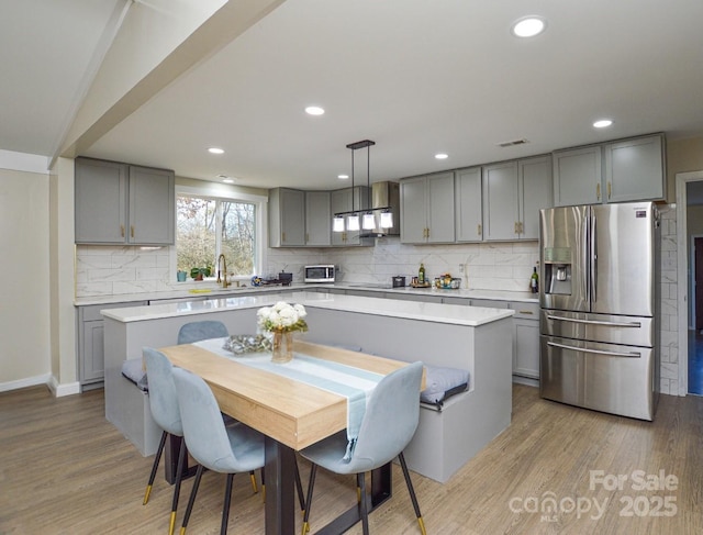 kitchen featuring a kitchen island, stainless steel fridge, light hardwood / wood-style floors, and decorative light fixtures