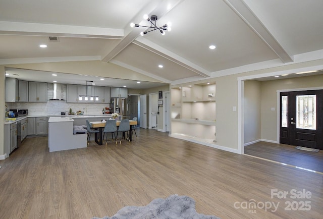 kitchen featuring gray cabinets, appliances with stainless steel finishes, a breakfast bar area, a center island, and wall chimney range hood