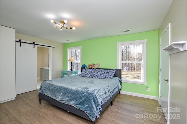 bedroom featuring hardwood / wood-style flooring, ensuite bathroom, a barn door, and a chandelier