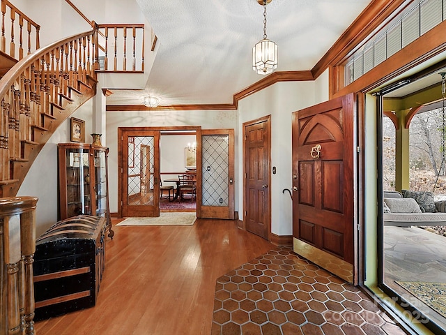 foyer entrance with wood-type flooring, ornamental molding, and a textured ceiling