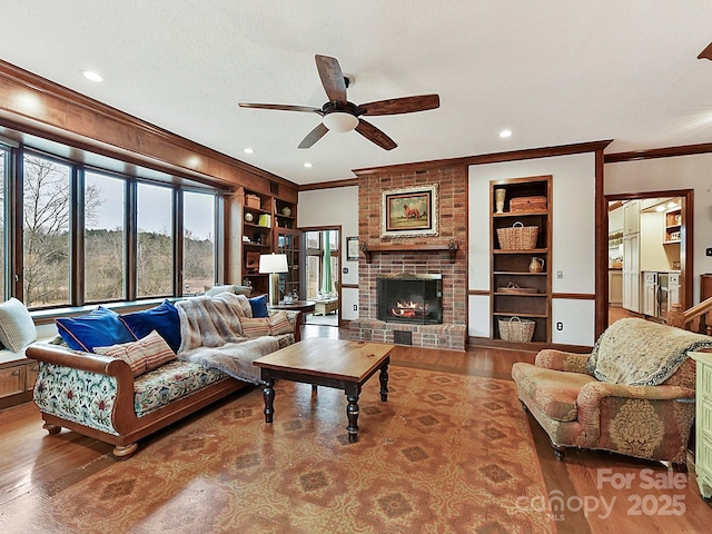 living room featuring built in shelves, ornamental molding, a fireplace, and wood-type flooring