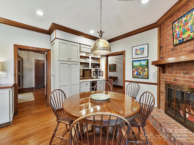 dining space featuring ornamental molding, wine cooler, a fireplace, and light hardwood / wood-style floors